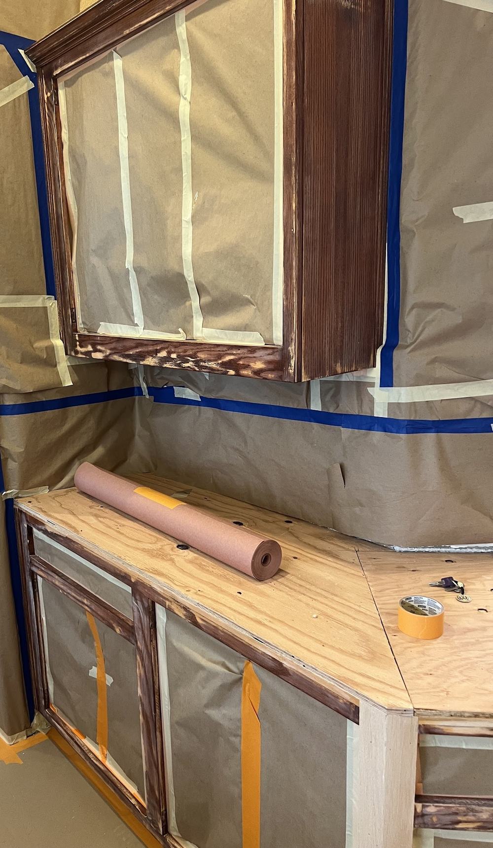 A kitchen masked for spraying: brown paper taped over the walls, counters and ceiling with blue tape lines.