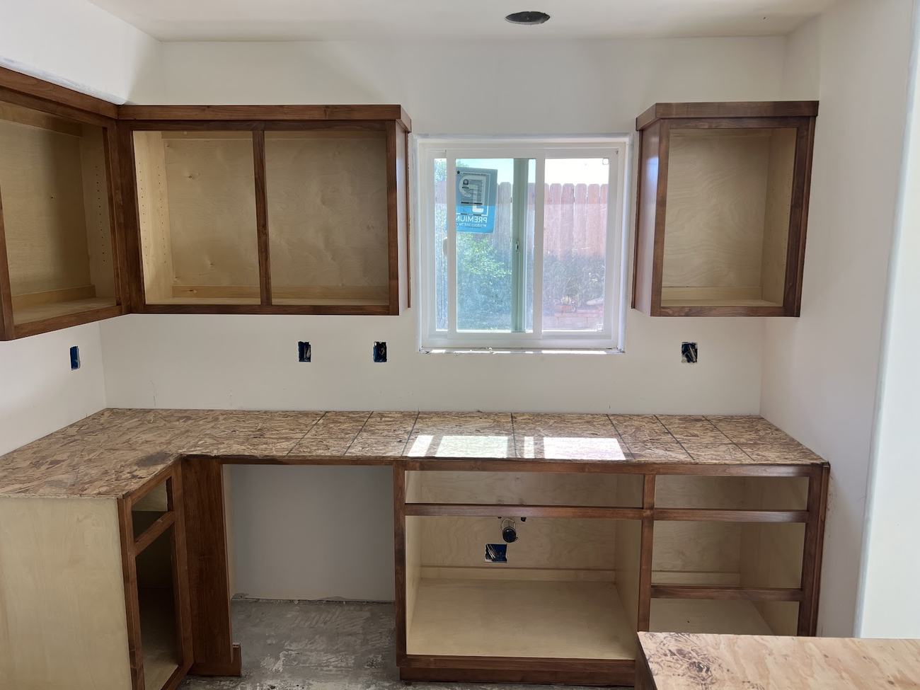 A kitchen with the cabinet doors removed and the boxes sanded back to bare wood, ready for finishing.