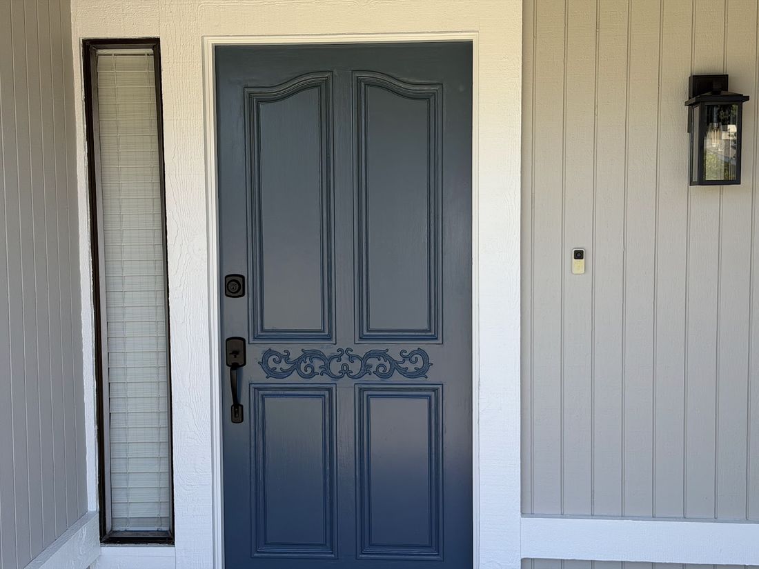 A panelled front door finished in slate blue against white board siding, with a glass sidelight.