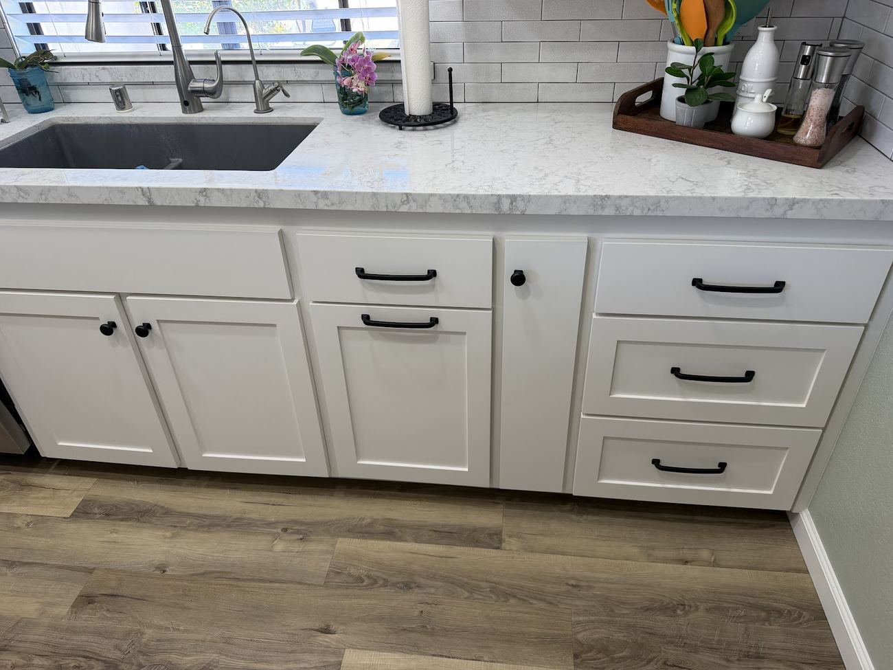 A finished kitchen with white cabinets, stone countertop and black hardware.